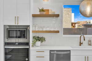 Kitchen with sink, appliances with stainless steel finishes, backsplash, light stone counters, and white cabinets