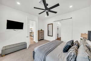 Bedroom featuring ceiling fan, a barn door, and light carpet