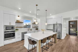 Kitchen featuring a breakfast bar, sink, white cabinetry, hanging light fixtures, and appliances with stainless steel finishes