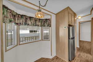 Kitchen with pendant lighting, stainless steel refrigerator, ornamental molding, light brown cabinets, and light hardwood / wood-style flooring