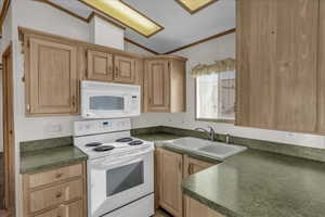 Kitchen with light brown cabinetry, lofted ceiling, sink, ornamental molding, and white appliances