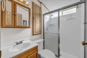 Bathroom featuring vanity, toilet, an enclosed shower, and a textured ceiling