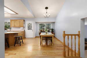 Dining space with vaulted ceiling with skylight, an inviting chandelier, and light hardwood / wood-style floors