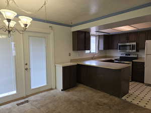 Kitchen with sink, hanging light fixtures, dark brown cabinetry, kitchen peninsula, and stainless steel appliances