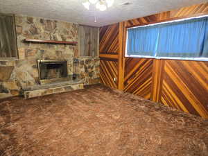 Unfurnished living room featuring a stone fireplace, wooden walls, a textured ceiling, and carpet flooring