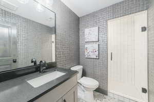 Bathroom with a tile shower, tile walls, vanity, and toilet