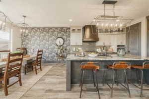 Kitchen featuring sink, light stone counters, a notable chandelier, pendant lighting, and wall chimney range hood