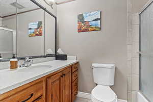 Full bathroom with vanity, bath / shower combo with glass door, tile patterned floors, and toilet