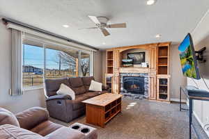 Living room featuring ceiling fan, a fireplace, carpet floors, and a textured ceiling