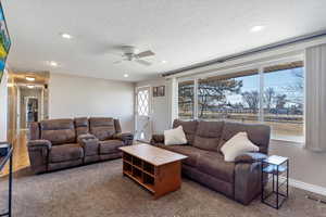 Carpeted living room featuring ceiling fan and a textured ceiling