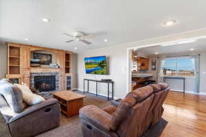 Living room featuring ceiling fan, light wood-type flooring, a textured ceiling, and a fireplace