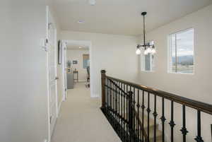 Corridor with light colored carpet and a notable chandelier