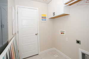 Washroom featuring washer hookup, electric dryer hookup, light tile patterned floors, and cabinets