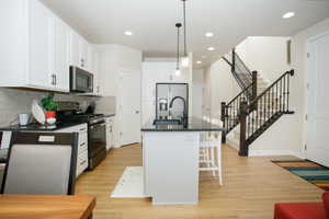 Kitchen with sink, white cabinets, hanging light fixtures, stainless steel appliances, and a center island with sink