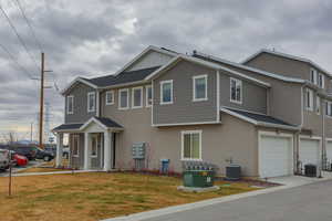 View of front of home featuring central AC, a garage, and a front lawn