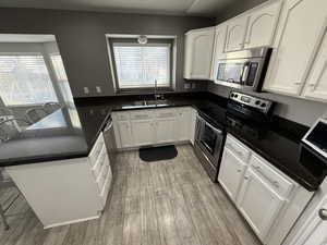 Kitchen with appliances with stainless steel finishes, sink, dark stone countertops, white cabinets, and light hardwood / wood-style flooring