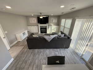 Living room with a tiled fireplace, ceiling fan, light hardwood / wood-style flooring, and a textured ceiling