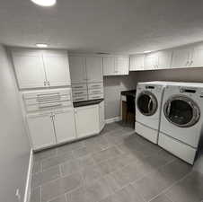 Laundry area with cabinets, light tile patterned floors, a textured ceiling, and washer and clothes dryer