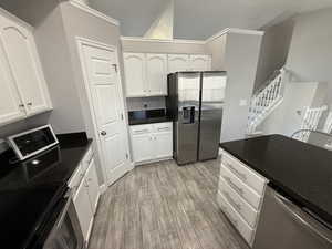 Kitchen with stainless steel appliances, light wood-type flooring, dark stone counters, and white cabinets