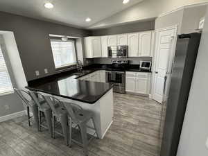 Kitchen featuring vaulted ceiling, appliances with stainless steel finishes, sink, kitchen peninsula, and light wood-type flooring