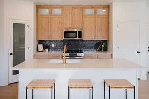 Kitchen featuring decorative backsplash, stainless steel appliances, a kitchen bar, and a center island with sink