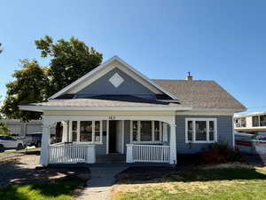 View of front of home with covered porch, a shingled roof, and a chimney