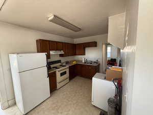 Kitchen with white appliances, light floors, light countertops, and under cabinet range hood
