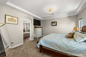 Carpeted bedroom featuring a tray ceiling and ensuite bath