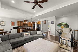 Living room featuring dark wood-type flooring, ceiling fan, a raised ceiling, and sink