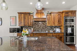 Kitchen featuring pendant lighting, custom exhaust hood, dark stone counters, and appliances with stainless steel finishes