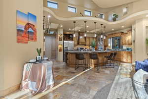 Kitchen featuring a breakfast bar area, hanging light fixtures, custom range hood, a towering ceiling, and stainless steel appliances