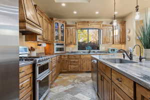 Kitchen featuring hanging light fixtures, custom exhaust hood, appliances with stainless steel finishes, and sink