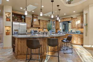 Kitchen featuring appliances with stainless steel finishes, stone tile floors, custom range hood, recessed lighting, and a large island with sink