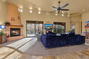 Living area featuring stone tile flooring, a towering ceiling, a ceiling fan, a glass covered fireplace, and recessed lighting