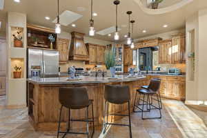 Kitchen featuring premium range hood, hanging light fixtures, stainless steel appliances, a kitchen bar, and a large island with sink