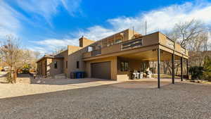Back of property featuring stucco siding, a balcony, an attached garage, gravel driveway, and a chimney