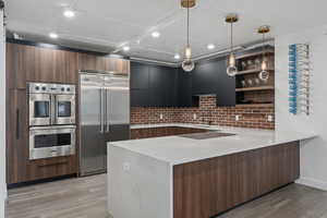 Kitchen featuring appliances with stainless steel finishes, pendant lighting, sink, LVP flooring, and kitchen peninsula with induction cooktop