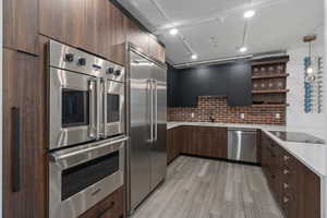 Kitchen with sink, light stone counters, appliances with stainless steel finishes, light hardwood / wood-style floors, and decorative backsplash