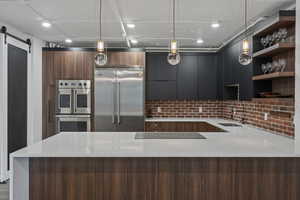 Kitchen with hanging light fixtures, appliances with stainless steel finishes, sink, and a metal barn door