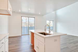 Kitchen featuring hardwood / wood-style flooring, white cabinetry, a kitchen island with sink, and sink