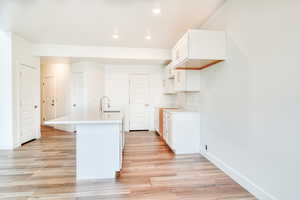 Kitchen with a kitchen island with sink, sink, white cabinets, and light hardwood / wood-style floors