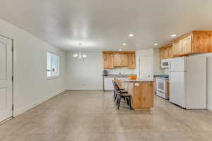 Kitchen featuring a breakfast bar, pendant lighting, light brown cabinetry, a center island, and white appliances