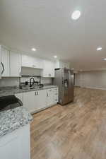 Kitchen featuring white cabinets, stainless steel fridge, range, light stone countertops, and light wood-type flooring