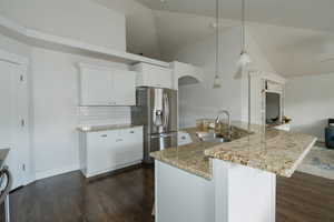 Kitchen featuring stainless steel refrigerator with ice dispenser, sink, white cabinetry, decorative light fixtures, and a kitchen island with sink