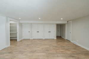 Unfurnished bedroom with multiple closets, light hardwood / wood-style flooring, and a textured ceiling