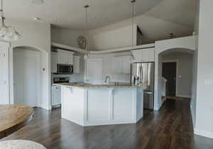 Kitchen featuring white cabinetry, an island with sink, appliances with stainless steel finishes, and decorative light fixtures