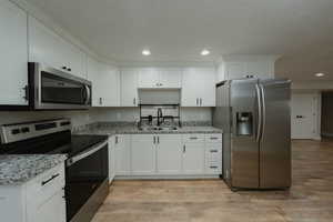 Kitchen featuring sink, stainless steel appliances, light stone countertops, white cabinets, and light wood-type flooring