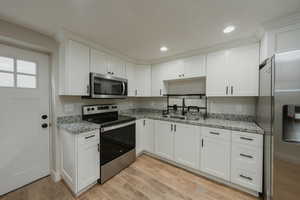 Kitchen with sink, white cabinetry, light wood-type flooring, appliances with stainless steel finishes, and light stone countertops