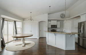 Kitchen featuring stainless steel appliances, white cabinetry, hanging light fixtures, and an island with sink