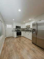 Kitchen featuring white cabinetry, appliances with stainless steel finishes, light stone countertops, and light hardwood / wood-style floors